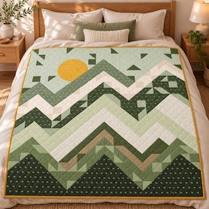 May include: A quilted blanket featuring a geometric mountain landscape pattern in shades of sage green, dark forest green, white, and tan. A solid yellow circle represents the sun in the upper left corner. The quilt has a mustard yellow border.