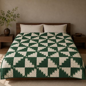 Könnte beinhalten: Eine Bettdecke mit einem geometrischen Muster aus abwechselnden dunkelgrünen und cremeweißen Stoffblöcken, die in einem gestuften, dreieckigen Design angeordnet sind. Die Decke ist mit einem Gittermuster gesteppt und bedeckt ein Bett mit zwei passenden rechteckigen Kissen.