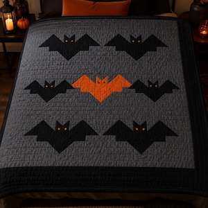 May include: A gray quilt featuring a repeating pattern of black bats with orange eyes, with a single orange bat with black eyes positioned in the center. The quilt has a solid black border and is stitched with a grid pattern throughout the fabric.