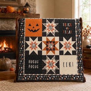Peut inclure: Une courtepointe sur le thème d'Halloween avec une palette de couleurs noir, orange et crème. Le motif comprend des étoiles, un visage de citrouille et les textes "TRICK OR TREAT", "HOCUS POCUS" et "EEK!" imprimés sur des blocs de tissu.
