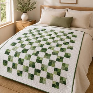 May include: A quilt featuring a checkerboard pattern of white squares and various shades of green patterned squares. The quilt has a white border with a diamond-stitched quilted texture and a thin green edge, covering a bed with neutral bedding.