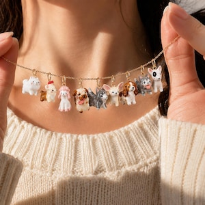 Può includere: Una collana a catena color oro con nove ciondoli smaltati in miniatura a forma di cane. I ciondoli raffigurano varie razze nei colori bianco, marrone, grigio e nero, ognuno fissato alla catena con un piccolo anellino color oro.
