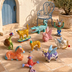 May include: A collection of small, colorful ceramic animal figurines including a leopard on a skateboard, a crocodile, a pink fairy frog, a rabbit on a skateboard, a turtle, a zebra, a spotted cat, a winged cow, and a red monkey.