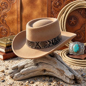 Puede incluir: Un sombrero de vaquero de fieltro color canela con un ala ancha y estructurada y una copa redondeada. El sombrero está decorado con una banda de patrón de piel de serpiente en marrón oscuro y negro que rodea la base de la copa del sombrero.