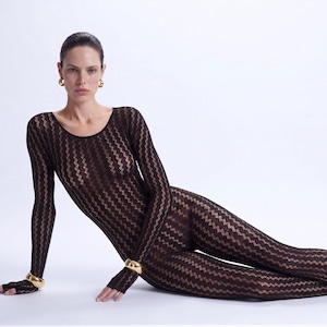 May include: A long-sleeved, full-length brown bodysuit featuring a vertical chevron knit pattern. The garment has a round neckline and is paired with gold-toned hoop earrings and thick gold-toned bracelets on each wrist, plus black pointed-toe heels.
