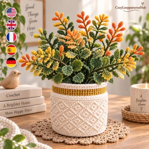 Puede incluir: Una planta de ganchillo con hojas verdes, amarillas y naranjas en una cesta blanca texturizada con una banda amarilla. La cesta presenta un patrón geométrico de diamantes y se asienta sobre un tapete de ganchillo beige. Texto CozyLooppatternsHub.