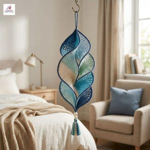 May include: A hanging spiral ornament crafted from crocheted yarn in shades of deep blue, light blue, and cream. The structure features an openwork pattern, a loop at the top for suspension, and a bottom accent with two white beads and a blue tassel.
