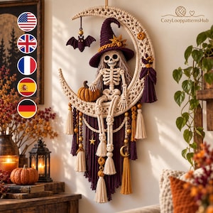 May include: A macrame wall hanging featuring a cream-colored crescent moon with a skeleton figure wearing a dark purple witch hat. The skeleton holds an orange pumpkin. The piece includes dark purple and cream tassels, beads, and a bat charm.
