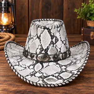 May include: A cowboy hat featuring a white and black snakeskin pattern throughout the crown and brim. The hat is accented with a black band adorned with silver-toned metal conchos, each displaying a central flower design and stitched edges.