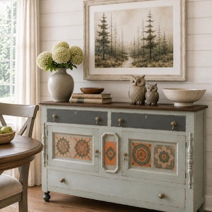 Peut inclure: Un buffet en bois bleu clair avec un plateau brun foncé, deux tiroirs supérieurs et quatre portes de placard inférieures ornées de motifs mandala orange et vert. Le meuble possède de petits boutons en laiton et repose sur quatre pieds.