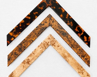 May include: Three V-shaped picture frame corner samples arranged vertically. The top sample features a glossy dark brown and black tortoiseshell pattern. The middle sample has a textured medium brown burl wood grain. The bottom sample is a light tan burl wood.