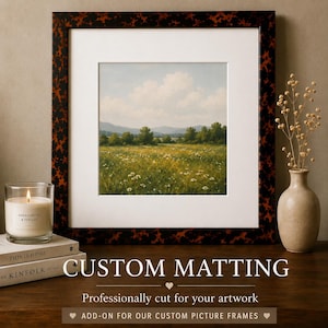 May include: A square landscape painting in a dark tortoiseshell frame with a white mat. The artwork depicts a green meadow with wildflowers, trees, and distant mountains under a cloudy sky. Text reads CUSTOM MATTING, Professionally cut for your artwork.