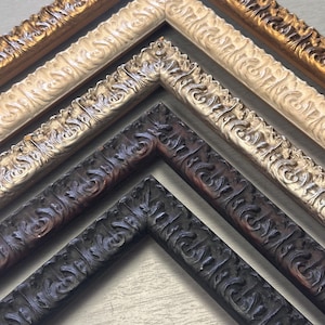 Könnte beinhalten: Eine Ansammlung von vier ineinander verschachtelten Bilderrahmen mit verzierten, erhabenen Schnörkelmustern. Die Rahmen sind in verschiedenen Farben gehalten, darunter Metallic-Gold, Cremeweiß, Silber und ein dunkler, verwitterter Holzton.
