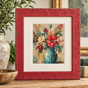 Puede incluir: Una impresión cuadrada enmarcada que muestra la pintura de un jarrón color verde azulado lleno de un ramo vibrante de flores rojas, blancas y rosas. El marco es de madera roja texturizada y desgastada con un patrón de hojas talladas y un paspartú.