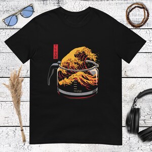 Könnte beinhalten: Ein schwarzes Kurzarm-T-Shirt mit einem Grafikdruck einer Glaskaffeekanne, die mit einer großen, stilisierten orangefarbenen und gelben Welle gefüllt ist. Das Design enthält japanischen Text in einem roten Kasten und Messmarkierungen.