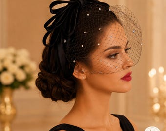 Könnte beinhalten: Ein schwarzer Fascinator mit einer großen Satinschleife und einem Netzschleier, der mit kleinen, klaren Kristallen besetzt ist. Der Schleier bedeckt den oberen Teil des Gesichts und das Kopfstück wird durch ein strukturiertes schwarzes Band gehalten.