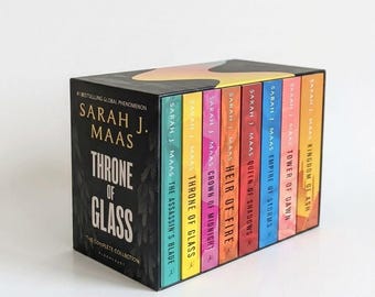 以下が含まれることがあります： サラ・J・マース著『Throne of Glass: The Complete Collection』のブックセット。黒い外箱には金色の文字とグラフィックデザインが施されています。中には8冊の本が収められており、それぞれの背表紙には著者名とタイトルが記載されています。