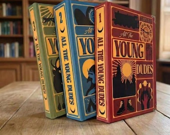 May include: Three hardcover books titled All The Young Dudes, numbered one through three. The red, blue, and green covers feature graphic illustrations including a train, a sun, a deer, and boots, with bold yellow text and decorative borders.