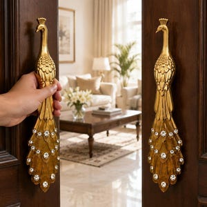 Peut inclure: Une paire de poignées de porte en métal doré en forme de paon. Chaque poignée présente une figure d'oiseau détaillée avec une longue queue en éventail ornée de cristaux circulaires transparents. Les poignées sont fixées sur des portes en bois brun.
