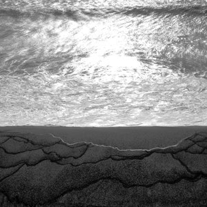 May include: A black and white photo of a beach with waves crashing on the shore. The sand is wet and has a pattern of lines.