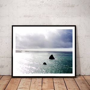 K&ouml;nnte beinhalten: Ein gerahmtes Foto einer Meereslandschaft mit einer dunklen, felsigen Insel in der Ferne. Der Himmel ist bedeckt mit grauen Wolken und das Wasser hat eine tiefblaue Farbe.