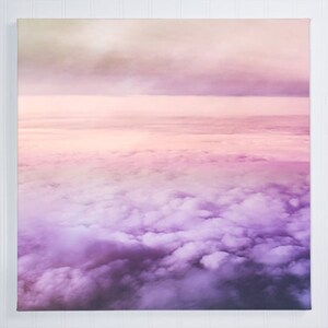 May include: A photograph of a pink and purple sky with fluffy white clouds. The clouds are layered and create a gradient effect from pink to purple.