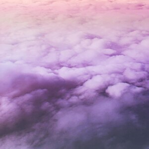 May include: A close-up view of a sky filled with fluffy white clouds, with a gradient of pink and purple hues.