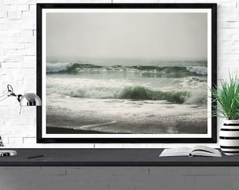 May include: A framed photograph of a misty ocean scene with waves crashing on a sandy beach. The waves are a vibrant green colour, and the sky is a soft grey.