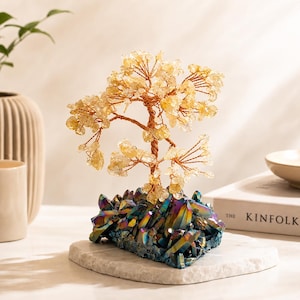 May include: A decorative tree sculpture featuring copper wire branches adorned with small, translucent yellow citrine-like crystal chips. The tree is anchored to a base of iridescent, multi-colored titanium-coated quartz crystal clusters.
