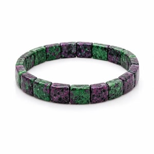 May include: A stretch bracelet composed of square-shaped beads made from a mottled stone material. The beads feature a distinct colour pattern of deep magenta and vibrant green with small black speckles throughout the polished surface.