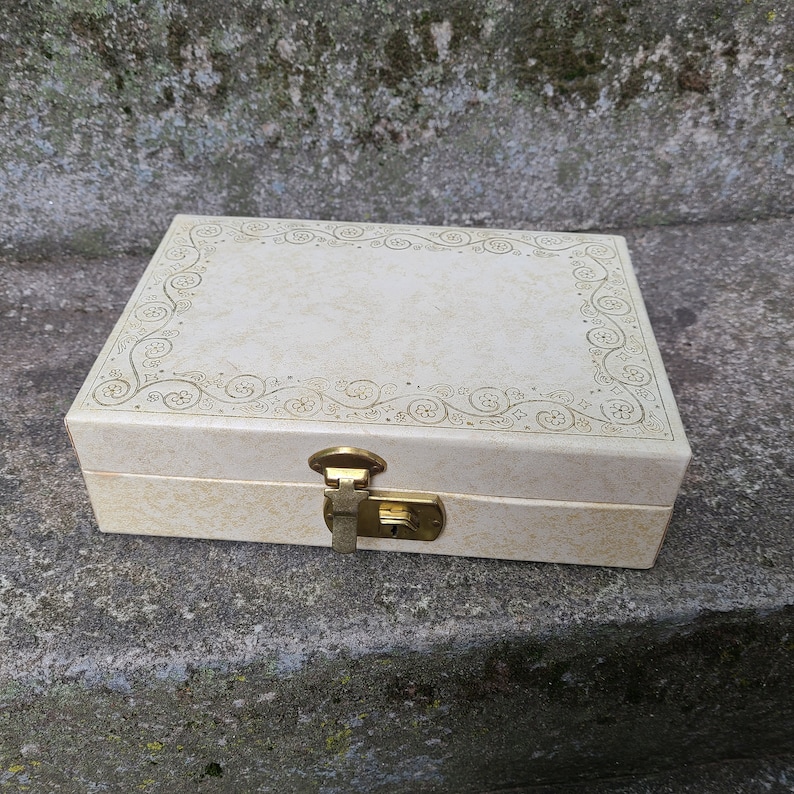 May include: A white jewelry box with a gold latch and a decorative floral design around the edge.