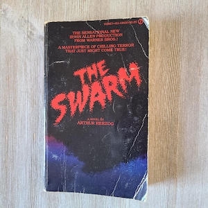 May include: A vintage paperback book titled "The Swarm" by Arthur Herzog. The cover features the title in large, red, jagged letters against a dark background with blue and purple hues. The book is a Signet publication.