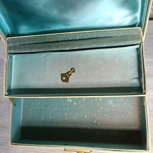 May include: A vintage jewelry box with a teal blue interior and a brass key. The box is made of a cream-colored material and has a brass latch.