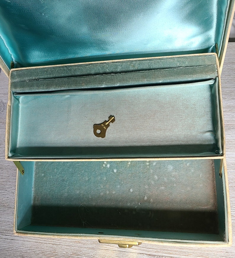 May include: A vintage jewelry box with a teal blue interior and a brass key. The box is made of a cream-colored material and has a brass latch.