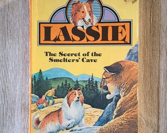 May include: Vintage "Lassie" book with a yellow cover. The title "Lassie" is in large orange letters. The book cover features an illustration of a collie dog, a mountain lion, and two boys. The book is titled "The Secret of the Smelters' Cave."