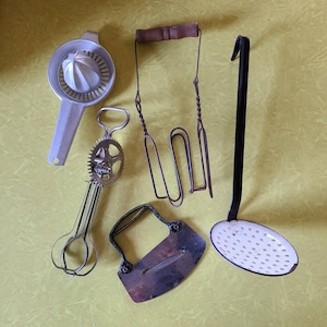 May include: A set of five vintage kitchen tools, including a citrus juicer, a hand-crank egg beater, a wire whisk, a metal cheese cutter, and a slotted spoon. The tools are all in various shades of silver and white.