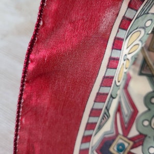 May include: A red silk scarf with a white and green geometric pattern. The scarf has a beaded trim.