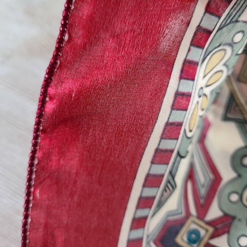 May include: A red silk scarf with a white and green geometric pattern. The scarf has a beaded trim.