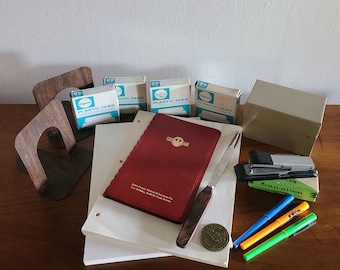 May include: A set of office supplies including a red notebook, a silver letter opener, a stapler, a box of plastic tabs, a wooden bookend, and a few pens and highlighters.