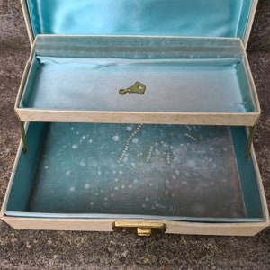 May include: A two-tiered jewelry box with a light blue velvet interior. The box has a gold-colored latch and a keyhole. The top tier is open and a small gold-colored key is visible inside.