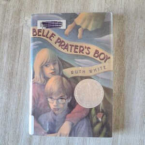 May include: A book titled "Belle Prater's Boy" by Ruth White. The cover features illustrations of two children and a woman, with a light blue and green background. A silver coin is on the cover.