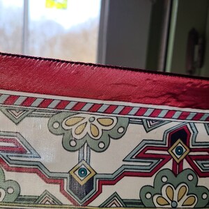 May include: A close-up of a red, white, and blue patterned fabric with a geometric design. The fabric has a red satin border.