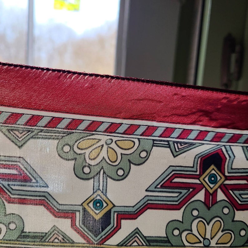 May include: A close-up of a red, white, and blue patterned fabric with a geometric design. The fabric has a red satin border.