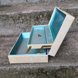 May include: A white and blue jewelry box with a hinged lid and a blue velvet interior. The box has a gold-colored latch and hinges.