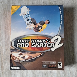May include: A box for the video game "Tony Hawk's Pro Skater 2" featuring a skateboarder mid-air. The game title is in large white letters with a silver oval border. The Activision logo is at the bottom left.