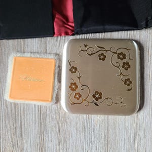 May include: A silver compact with a floral design and the word "Rimmel" embossed on the inside of the lid.