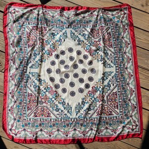 May include: A white silk scarf with a red border and a colorful geometric pattern. The pattern features a repeating design of circles, flowers, and geometric shapes.