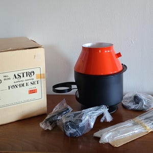 May include: A red and black fondue set with a safety-swing feature. The set is packaged in a box with the text "ASTRO Safety-Swing Fondue Set" printed on it.