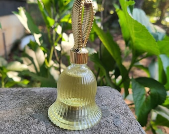 May include: A clear glass bottle with a gold bell-shaped base and a decorative gold top. The bottle is filled with a clear liquid.