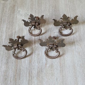 May include: Four antique metal drawer pulls with ornate leaf designs and a ring handle. The pulls are a dark brown color with a rustic finish.